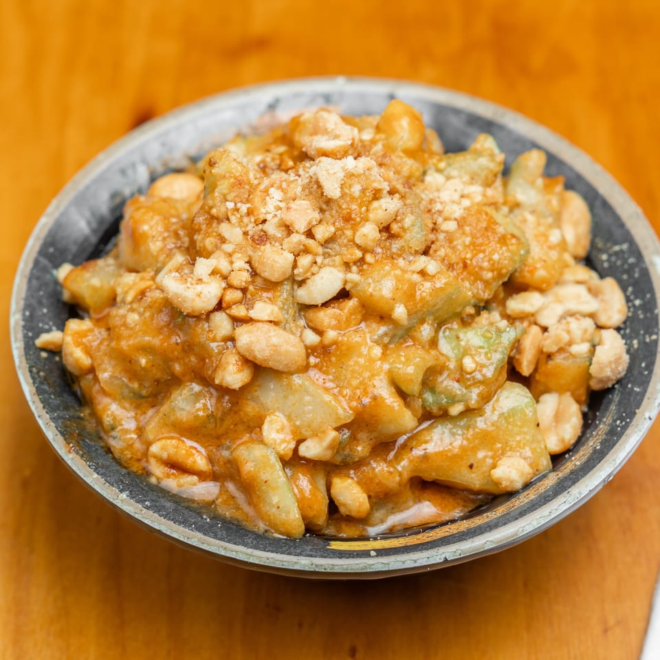 Close-up of saucy fried vegetables topped with crushed peanuts in a rustic bowl on a wooden table.