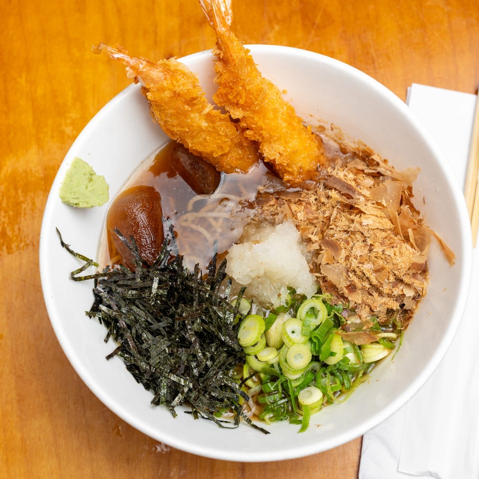 Japanese noodle bowl topped with fried shrimp, seaweed, scallions, mushrooms, grated radish, and bonito flakes, served with wasabi.