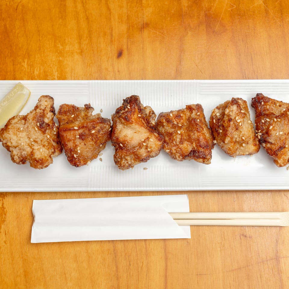 Sesame-sprinkled fried chicken pieces arranged on a white platter with a lemon wedge, chopsticks, and napkin.