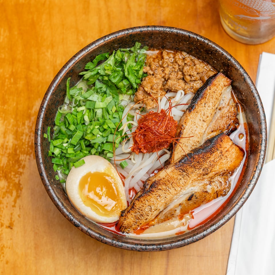 Overhead view of a ramen bowl topped with grilled pork, minced meat, soft-boiled egg, scallions, bean sprouts, and chili.