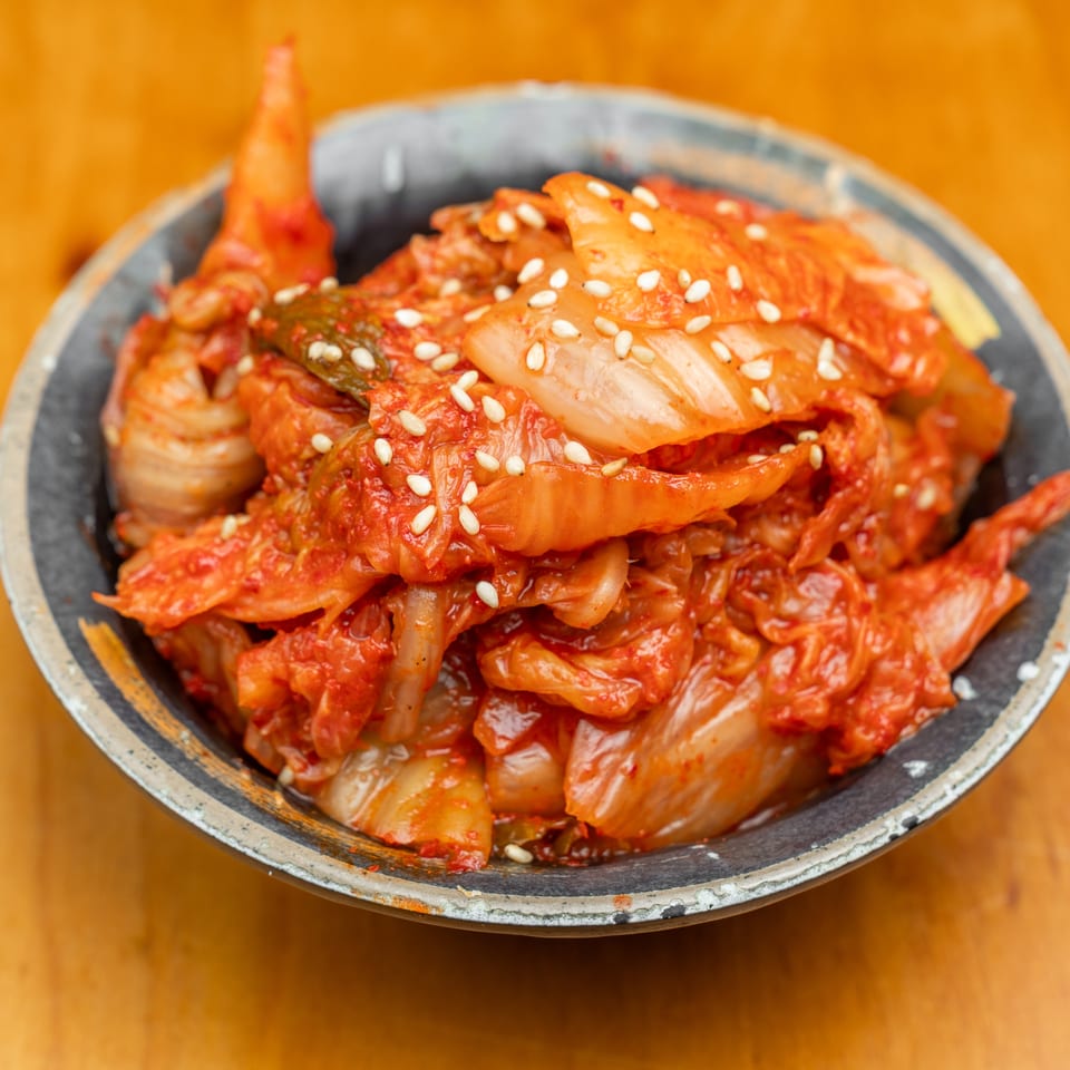Spicy red kimchi topped with sesame seeds in a rustic bowl on a wooden table.