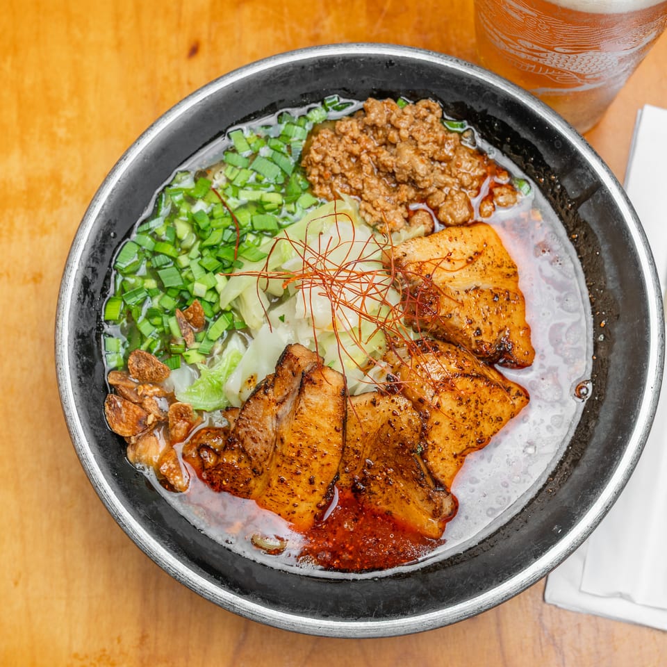 Overhead view of a spicy Asian noodle bowl topped with sliced grilled pork, minced meat, greens, vegetables, and chili threads.