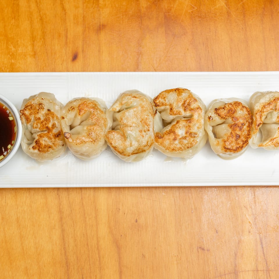 Golden-brown pan-fried dumplings arranged on a white platter with a small bowl of soy dipping sauce.