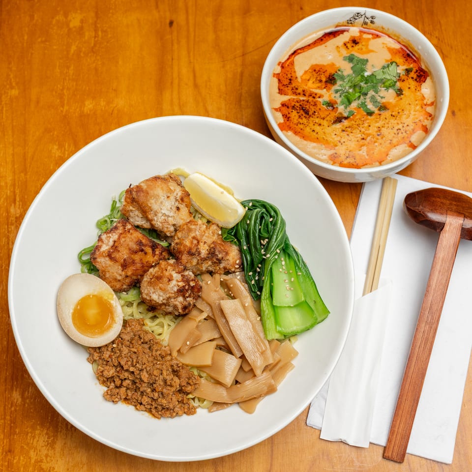 Top-down view of a Japanese noodle bowl with fried chicken, egg, vegetables, and ground meat beside spicy creamy soup and chopsticks.