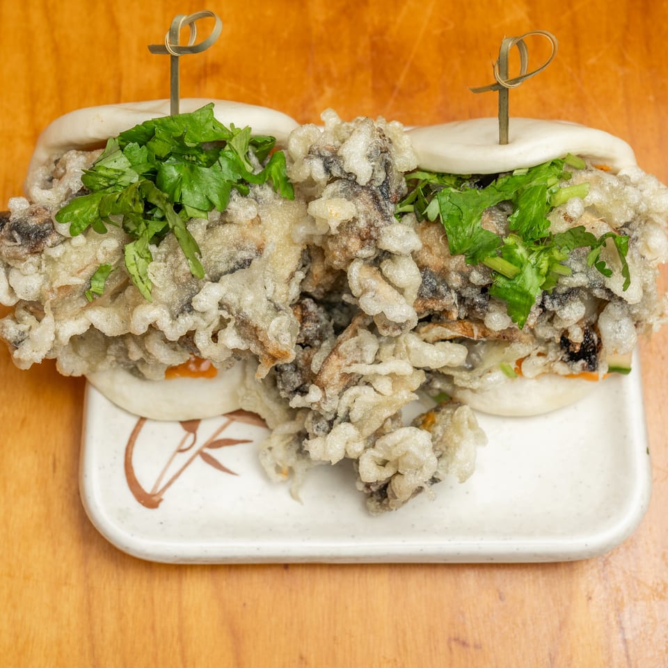 Two steamed bao buns filled with crispy fried mushrooms and topped with fresh cilantro on a plate.