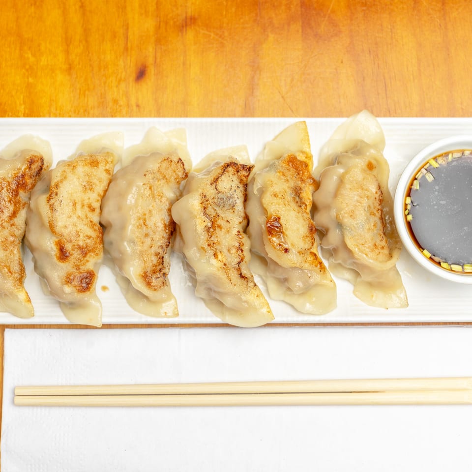 Pan-fried dumplings arranged on a white platter with dipping sauce and chopsticks on a wooden table.
